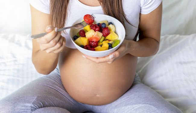 Schwangerschaft und gesunde Ernährung: schwangere Frau hält eine Schüssel mit frischem Obst in der Hand